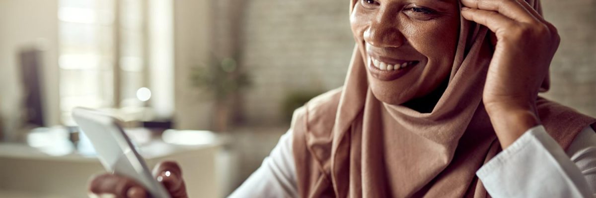 happy-black-islamic-businesswoman-using-cell-phone-text-messaging-while-working-office